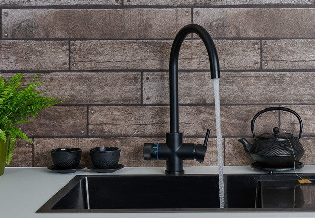 4-in-1 kraan in mat zwart met stromend water, thee-accessoires op een keukenblad — kokend, gekoeld en gezuiverd water uit één kraan van PureAqua