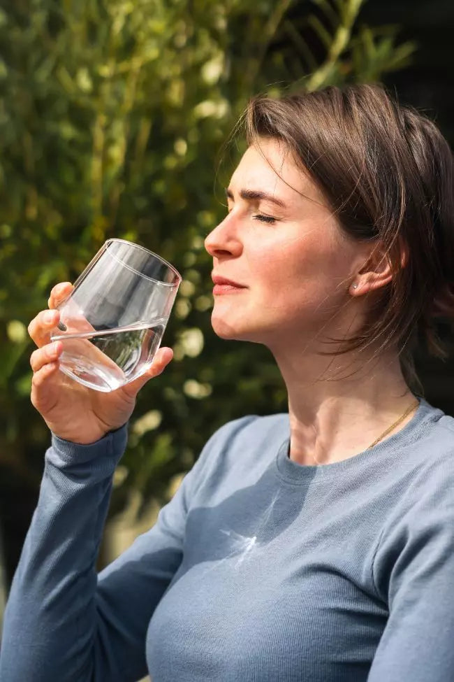 een vrouw die een glas zuiverwater drinkt in de zon
