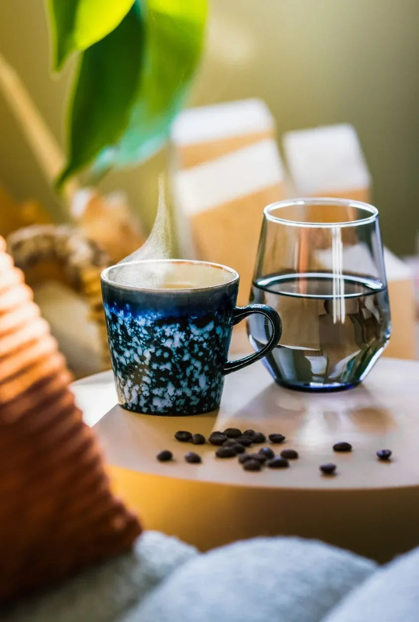 Sfeerbeeld bij de AquaPure kraan: dampende kop koffie en glas water met koffiebonen op tafel | PureAqua