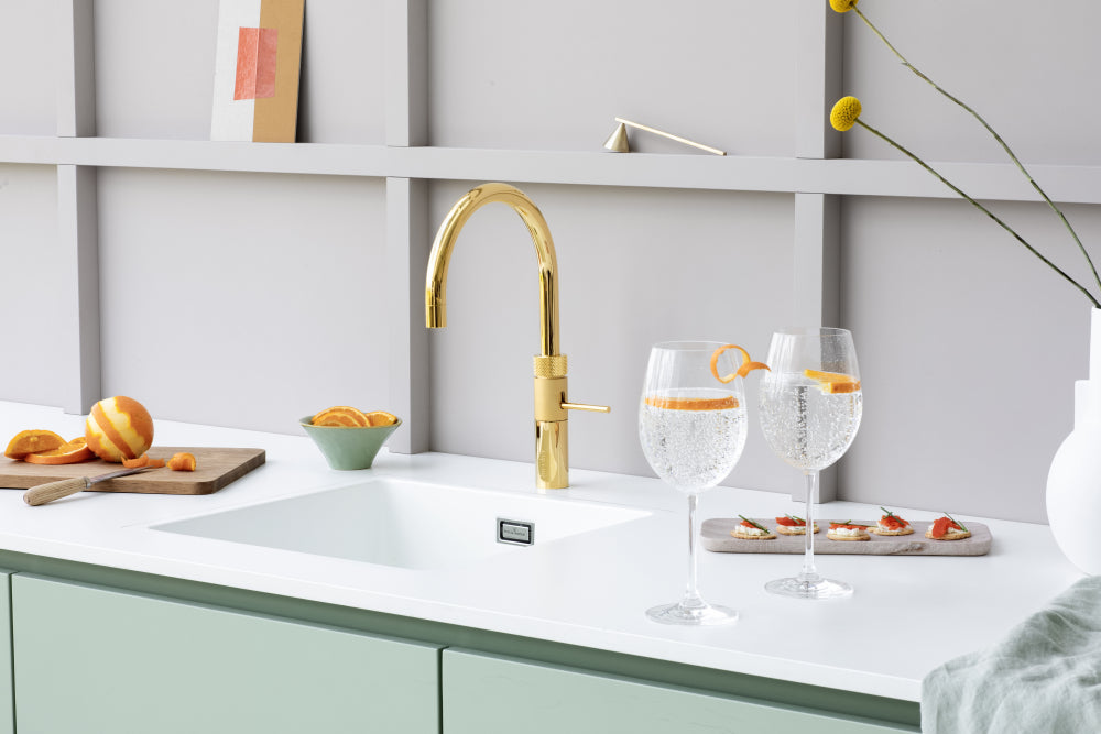 Gouden kokendwaterkraan Quooker in moderne keuken met bruisend water in glazen