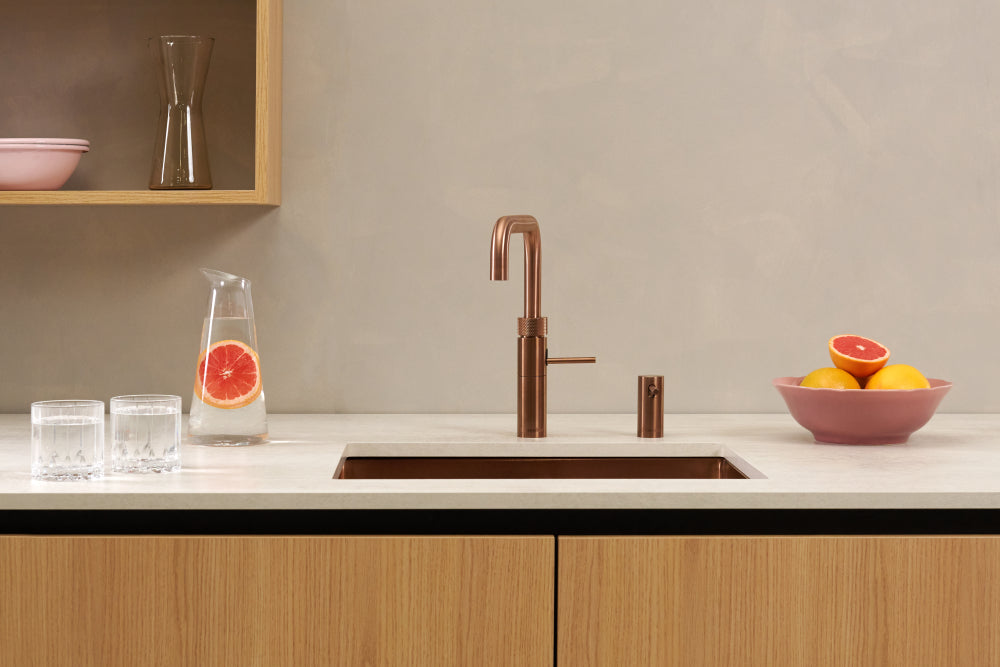 Quooker Fusion kokendwaterkraan in rosé koper, stijlvol geïntegreerd in een moderne keuken met fruit en glazen op het aanrecht