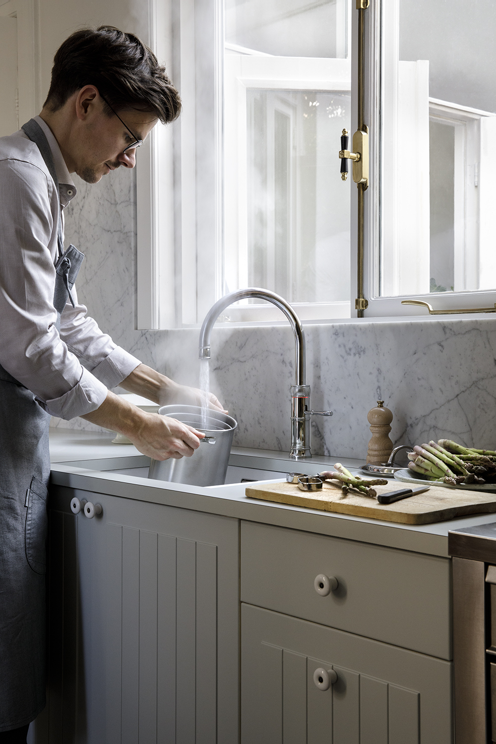 Man gebruikt chromen Quooker kokendwaterkraan in lichte keuken met marmeren achterwand om direct kokend water te tappen