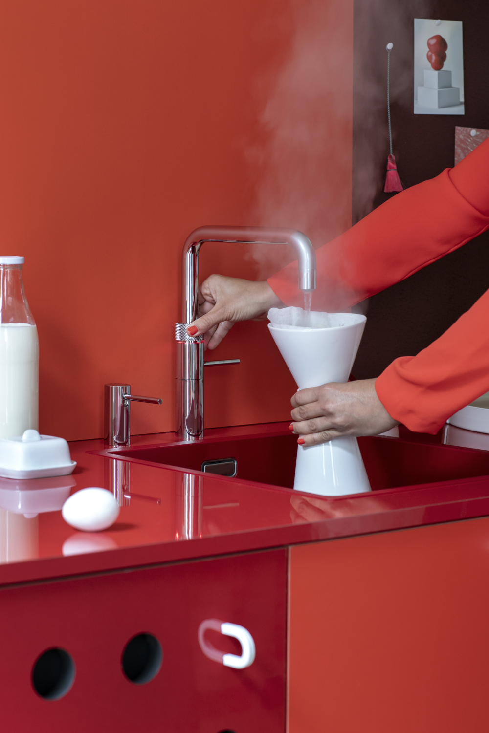 Vrouw tapt direct kokend water uit een chromen Quooker kraan in moderne rode keuken