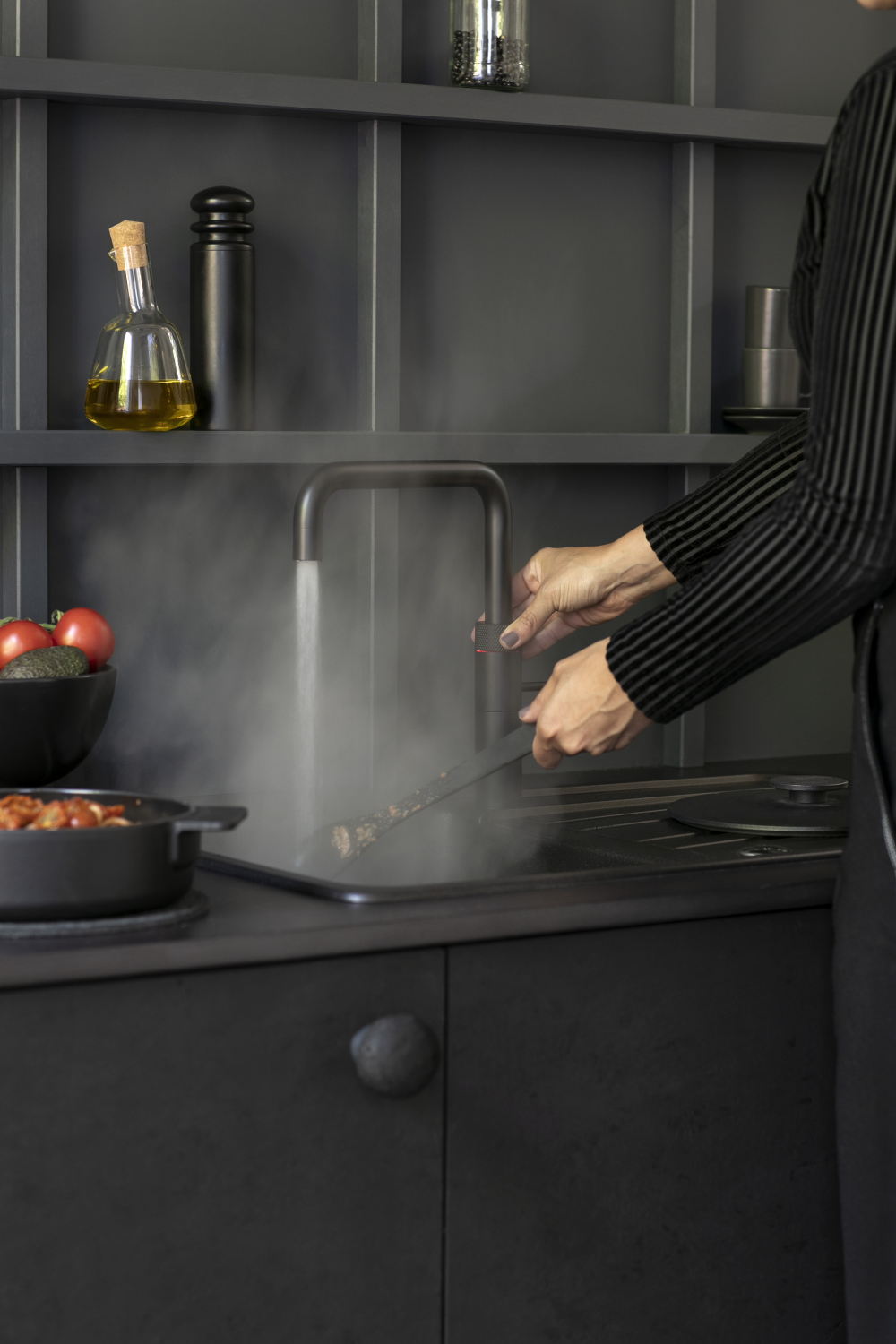 Persoon gebruikt zwarte Quooker kokendwaterkraan in moderne donkere keuken om direct kokend water te tappen