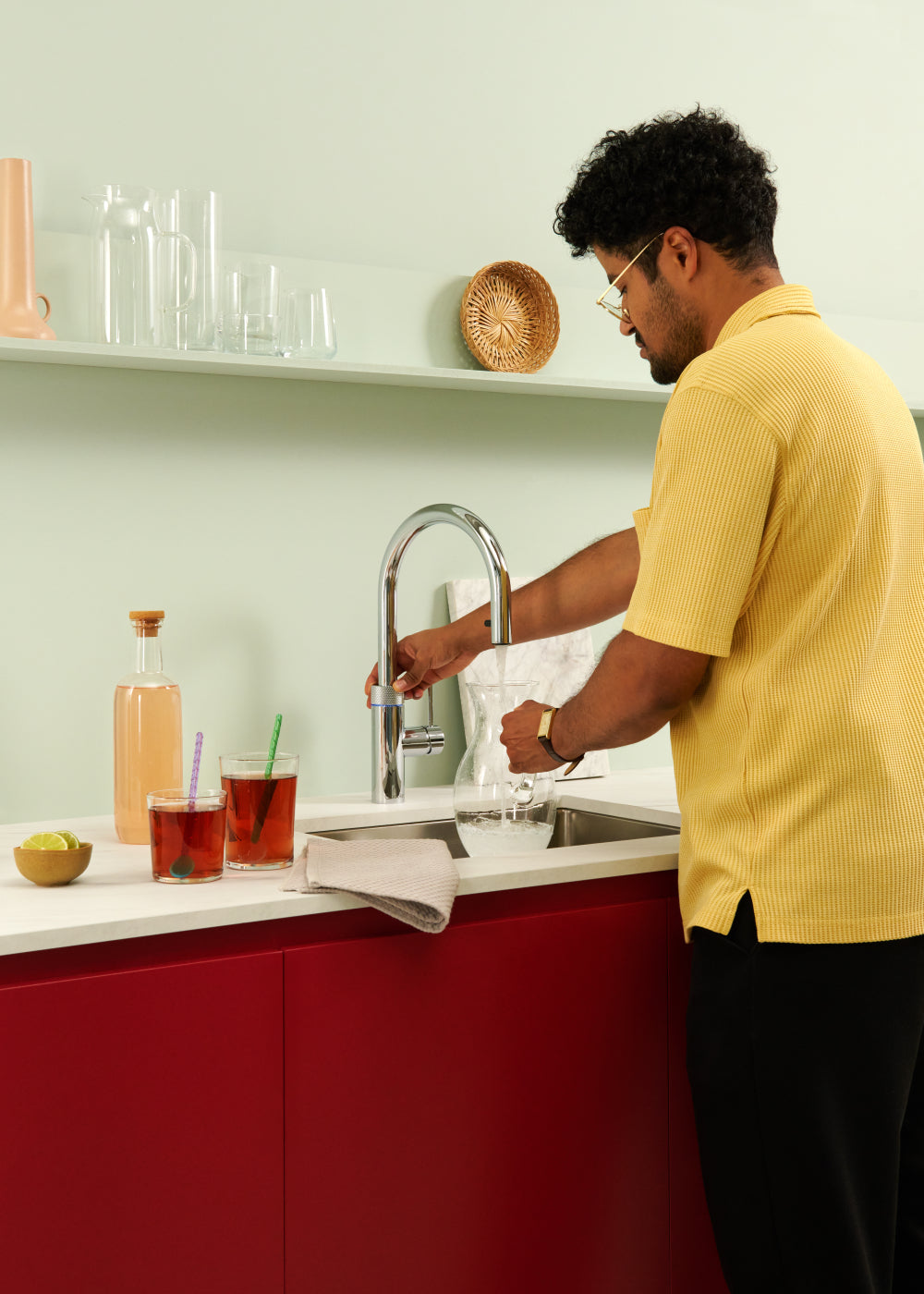 Man gebruikt Quooker kokendwaterkraan in moderne keuken om water in een karaf te tappen, met drankjes en citroen op het aanrecht