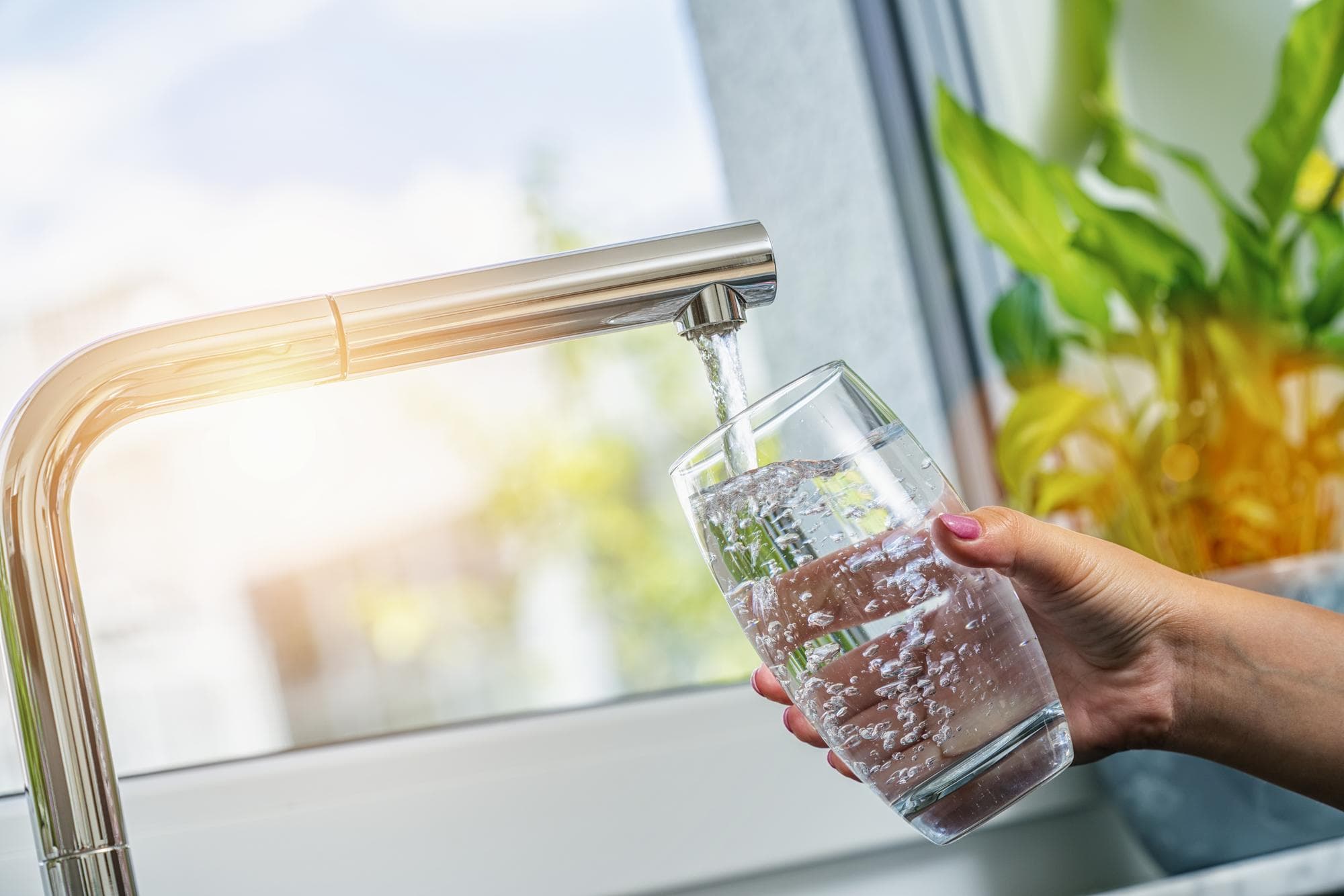 Hand vult glas met zuiver water uit moderne kraan aangesloten op reverse osmose waterfiltersysteem

