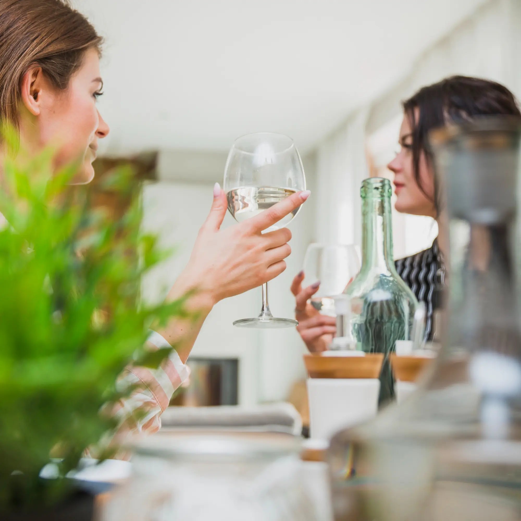 Twee vrouwen drinken schoon water uit wijnglazen aan tafel – symboliseert drinkwaterzekerheid en voorbereiding op noodsituaties met PureAqua.