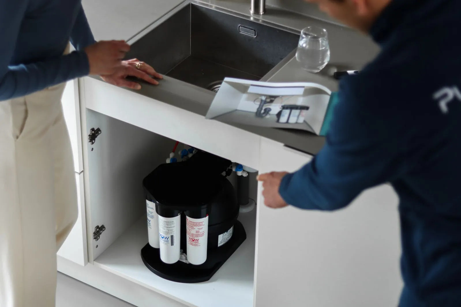Er wijst een man naar de geïnstalleerde drinkwaterfiltersysteem onder de wasbak